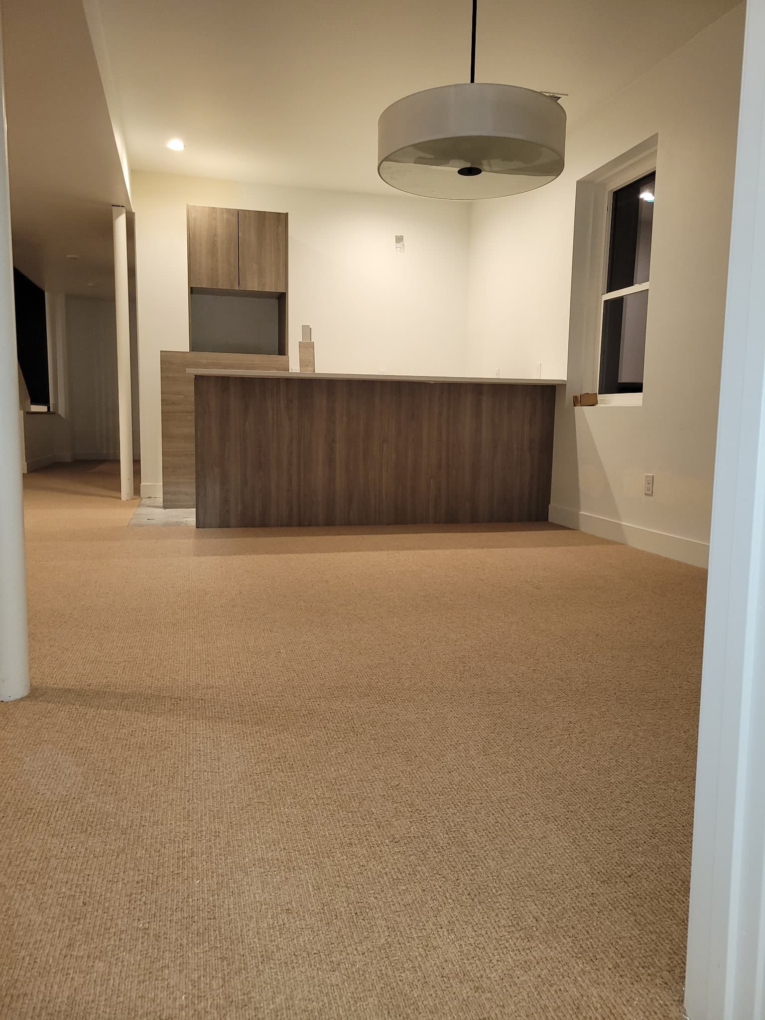 Modern interior with tan carpet, wood-paneled bar, and a large white drum pendant light.