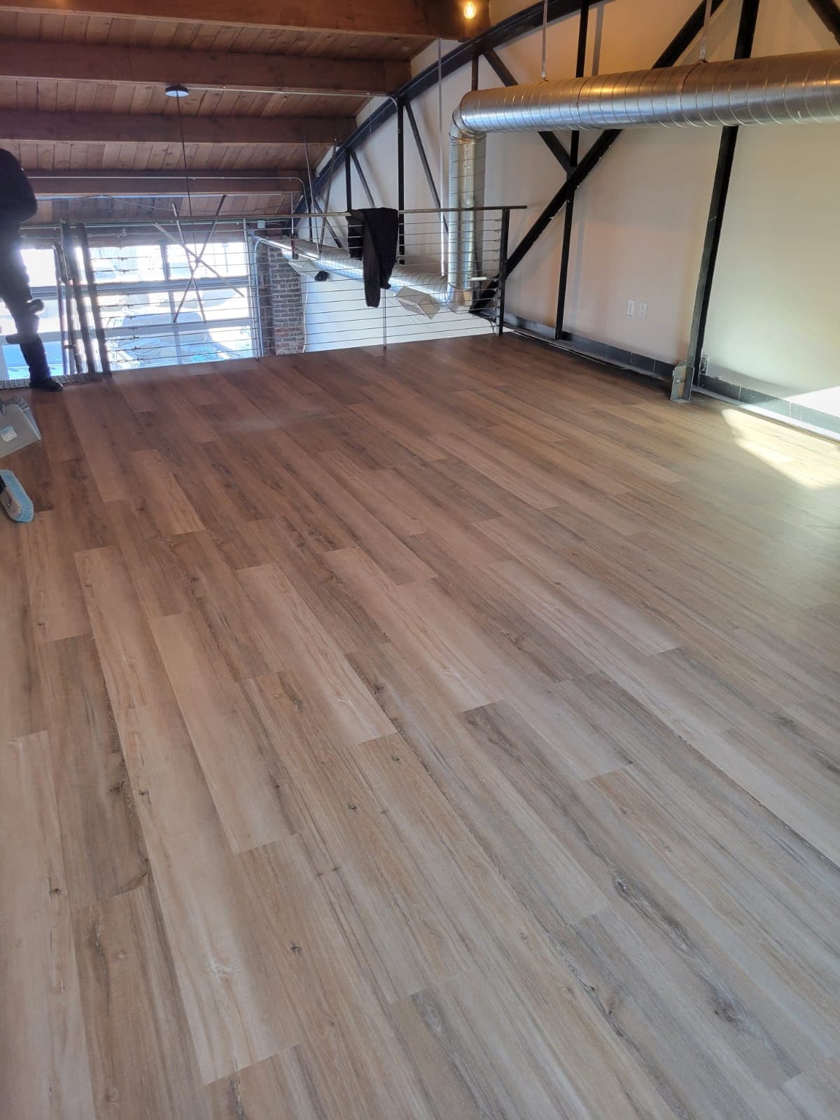 Light wood-look flooring installed in an open industrial loft with exposed beams and ductwork.