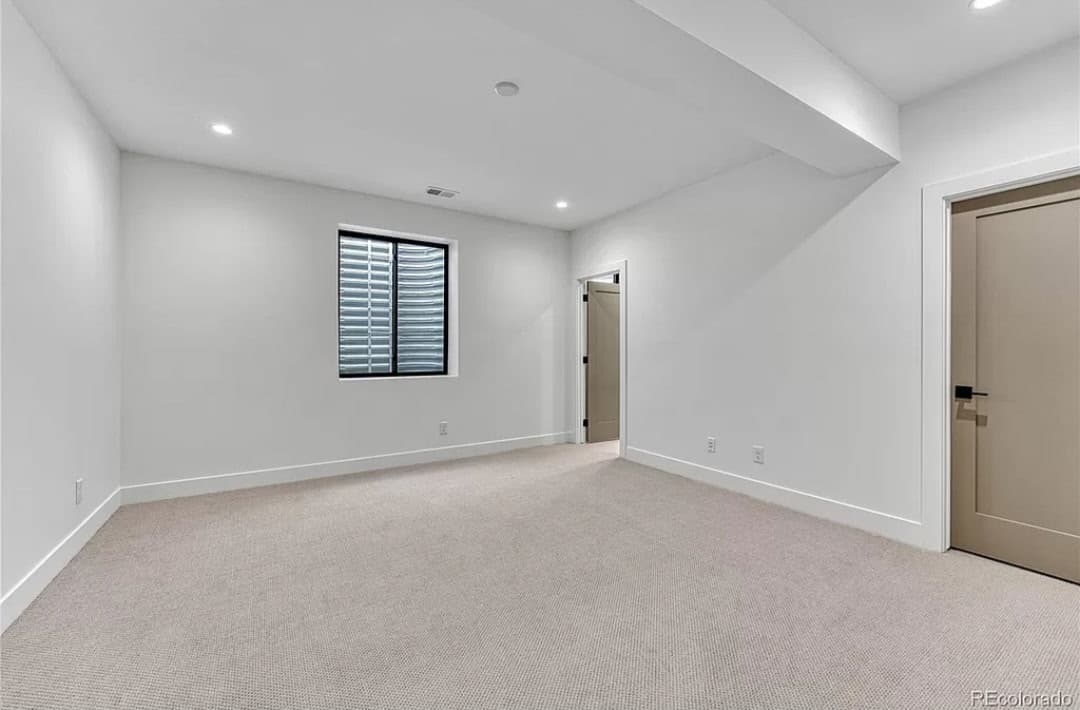 Modern empty room with white walls, neutral carpet, recessed lighting, and a small egress window.